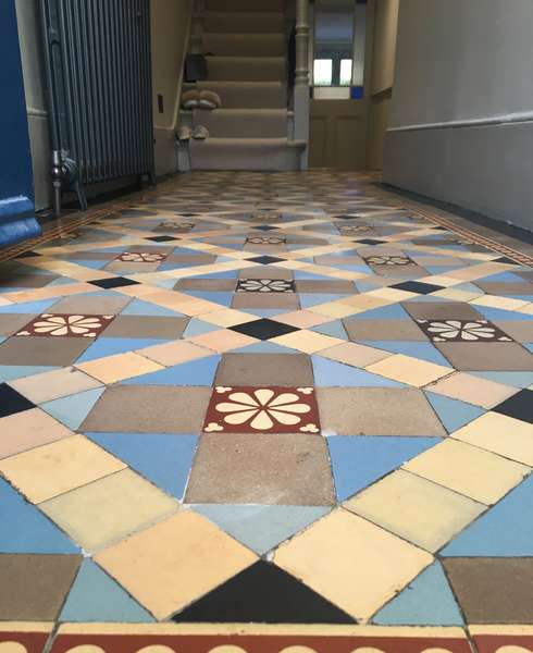 A closeup view of a cleaned Victorian floor containg encaustic and plain blue and buff tiles